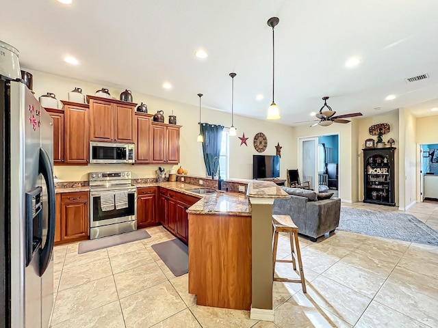 kitchen with kitchen peninsula, appliances with stainless steel finishes, a kitchen breakfast bar, sink, and hanging light fixtures