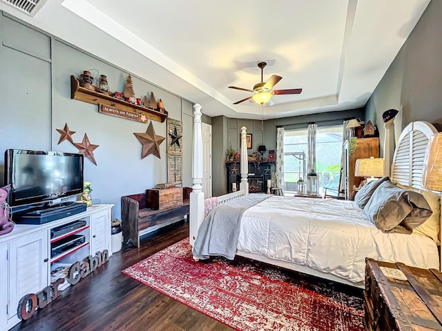 bedroom featuring ceiling fan, dark hardwood / wood-style flooring, ornate columns, and a tray ceiling