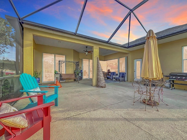 patio terrace at dusk featuring glass enclosure, ceiling fan, and area for grilling