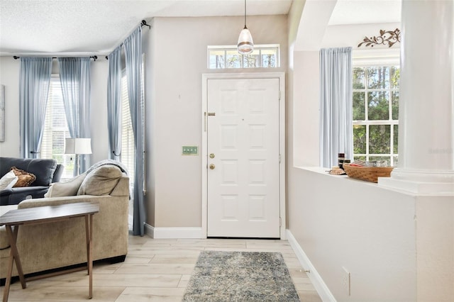 foyer entrance featuring a textured ceiling, light wood-type flooring, and ornate columns