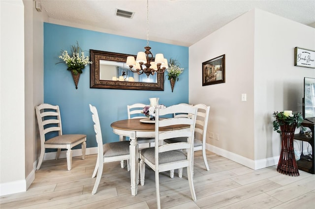 dining area with a notable chandelier, light wood-type flooring, and a textured ceiling