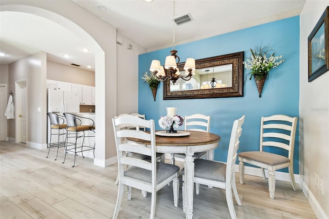 dining space with a textured ceiling, light hardwood / wood-style floors, and a notable chandelier