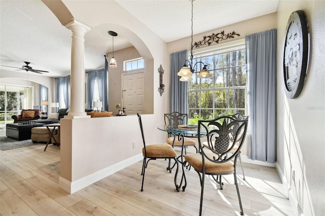 dining area featuring ceiling fan with notable chandelier, light hardwood / wood-style flooring, ornate columns, and a healthy amount of sunlight