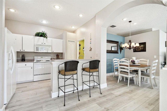 kitchen with pendant lighting, white cabinetry, white appliances, and light hardwood / wood-style floors