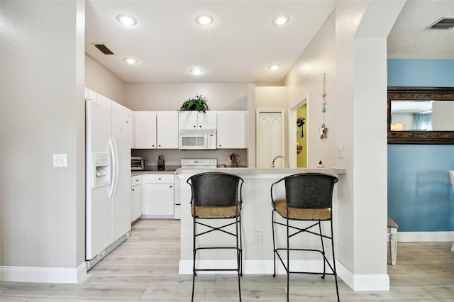 kitchen with white appliances, a kitchen breakfast bar, kitchen peninsula, light hardwood / wood-style floors, and white cabinetry