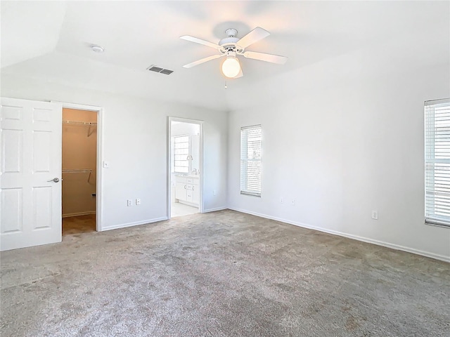 unfurnished bedroom featuring a walk in closet, ensuite bath, vaulted ceiling, ceiling fan, and a closet