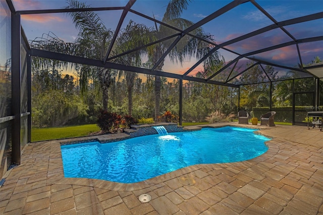 pool at dusk with a lanai, a patio area, and pool water feature