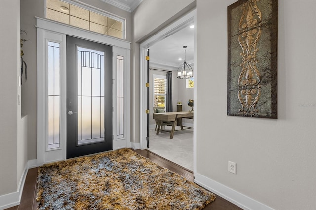 foyer entrance with hardwood / wood-style floors, crown molding, and a chandelier