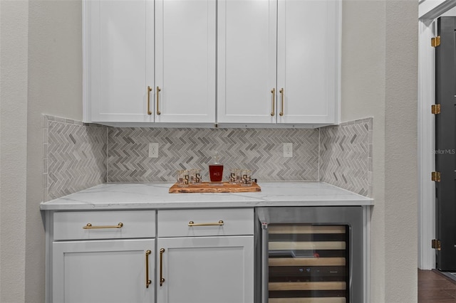 bar with decorative backsplash, light stone countertops, white cabinets, and beverage cooler