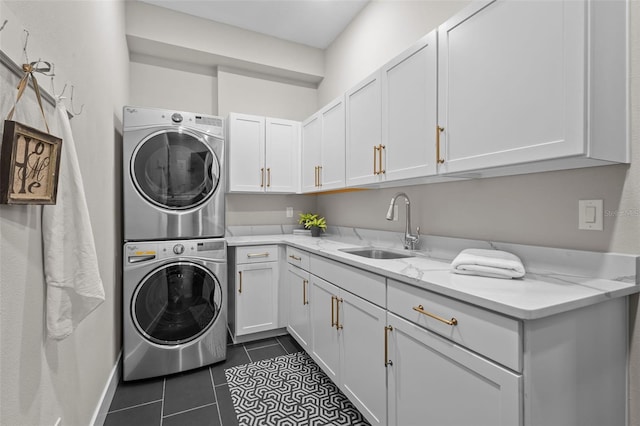 clothes washing area featuring dark tile patterned flooring, cabinets, stacked washing maching and dryer, and sink