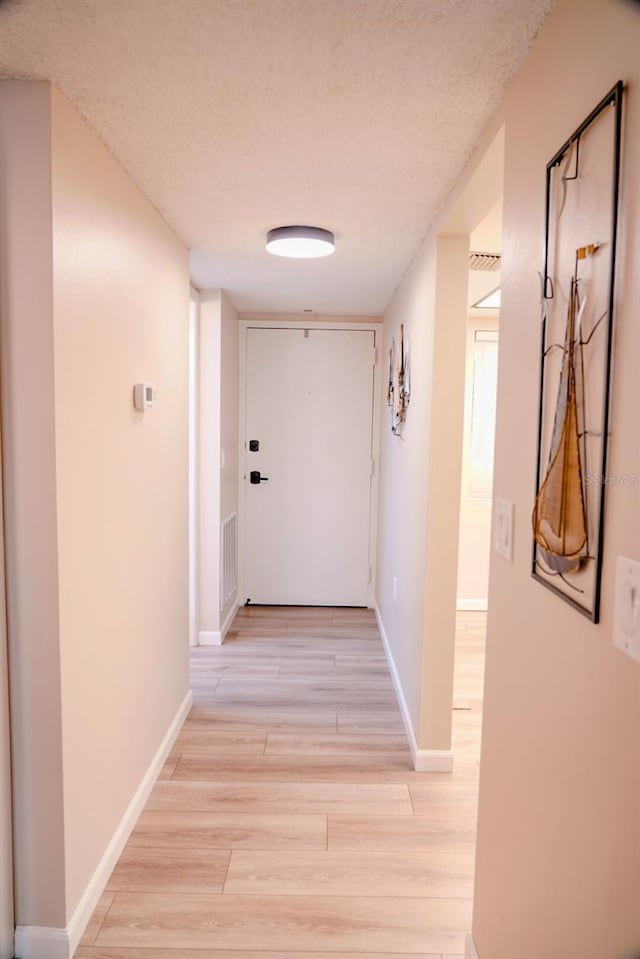 corridor with a textured ceiling and light wood-type flooring