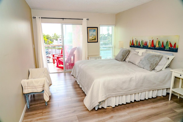 bedroom with access to exterior, a textured ceiling, and light hardwood / wood-style floors