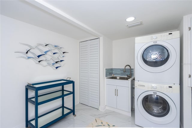 washroom with cabinets, stacked washer / dryer, and sink