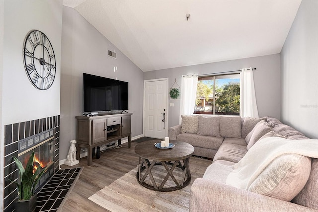 living room with a tiled fireplace, wood-type flooring, and lofted ceiling