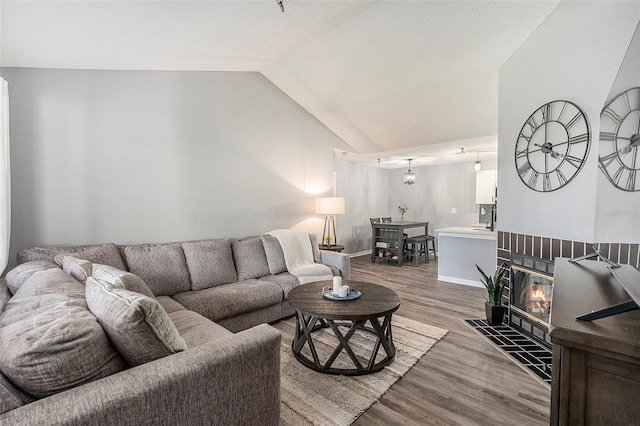 living room featuring a fireplace with flush hearth, vaulted ceiling, baseboards, and wood finished floors