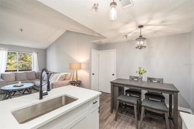 kitchen with visible vents, light countertops, hanging light fixtures, white cabinets, and a sink