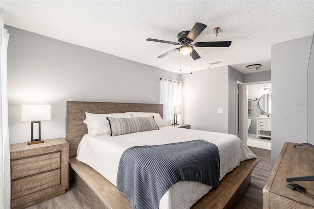 bedroom featuring a textured ceiling, ceiling fan, wood finished floors, visible vents, and ensuite bath