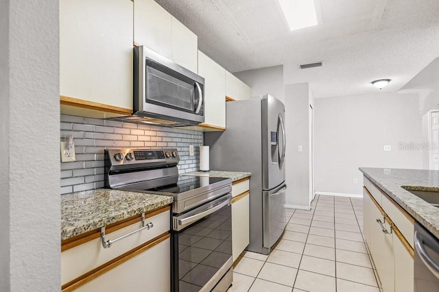 kitchen featuring appliances with stainless steel finishes, tasteful backsplash, light stone counters, a textured ceiling, and white cabinetry