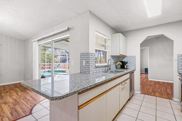 kitchen featuring dishwasher, sink, light tile patterned flooring, kitchen peninsula, and white cabinets