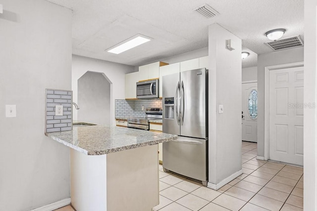 kitchen featuring white cabinets, light tile patterned flooring, kitchen peninsula, and appliances with stainless steel finishes