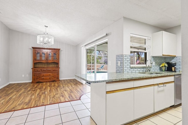 kitchen with sink, kitchen peninsula, light hardwood / wood-style floors, decorative light fixtures, and white cabinets