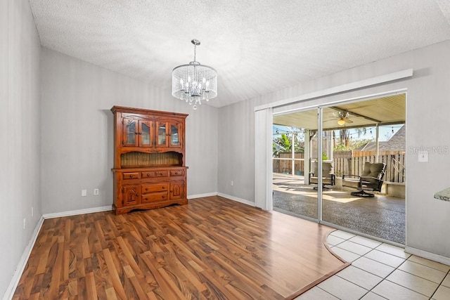 unfurnished room with ceiling fan with notable chandelier, a textured ceiling, and light hardwood / wood-style flooring