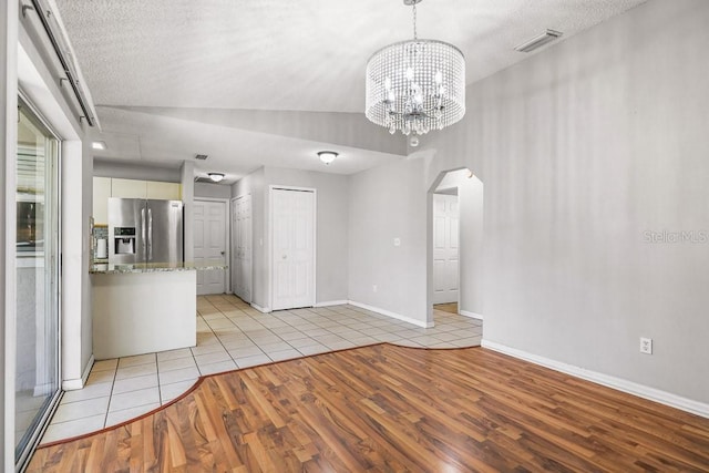 unfurnished living room with a textured ceiling, light hardwood / wood-style floors, an inviting chandelier, and vaulted ceiling