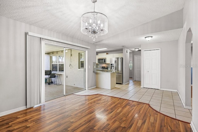 unfurnished living room with a notable chandelier, light hardwood / wood-style floors, and a textured ceiling