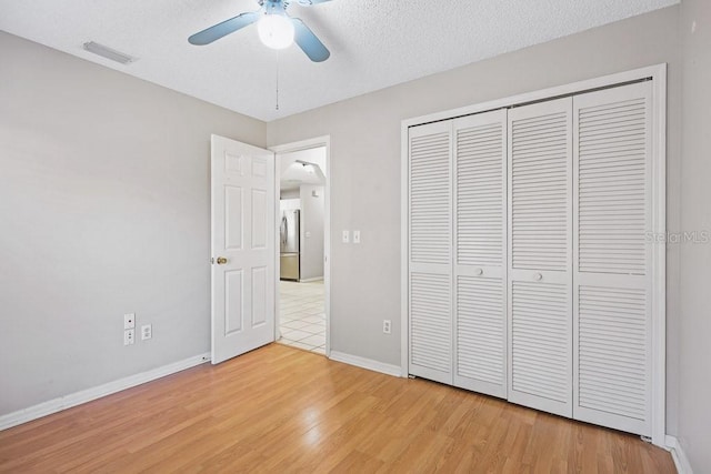 unfurnished bedroom with a textured ceiling, ceiling fan, wood-type flooring, stainless steel refrigerator, and a closet