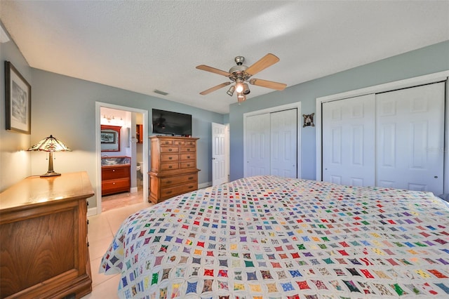 bedroom with two closets, ensuite bath, ceiling fan, light tile patterned floors, and a textured ceiling