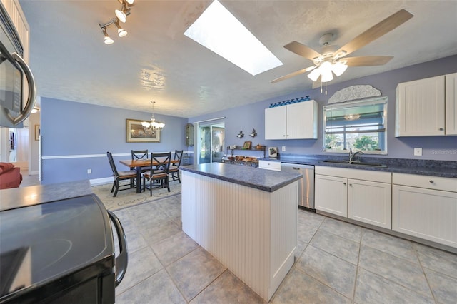 kitchen featuring a skylight, white cabinetry, sink, stainless steel appliances, and ceiling fan with notable chandelier