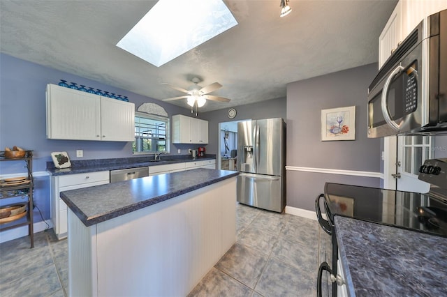 kitchen featuring appliances with stainless steel finishes, a skylight, ceiling fan, a center island, and white cabinetry