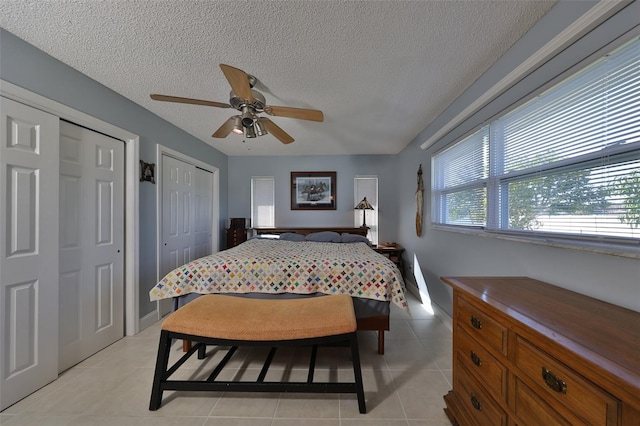 bedroom with multiple closets, ceiling fan, light tile patterned floors, and a textured ceiling