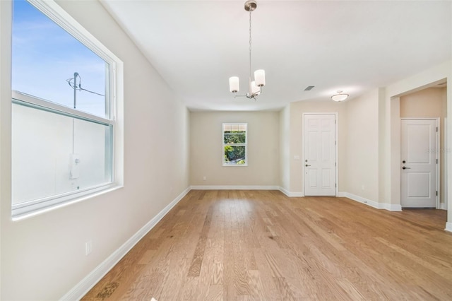 unfurnished room with a chandelier and light wood-type flooring