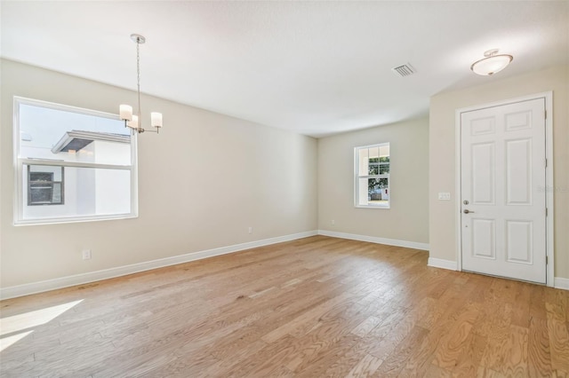 empty room with an inviting chandelier and light hardwood / wood-style flooring