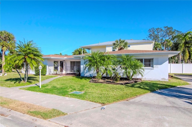 view of front of home featuring fence, a front lawn, and stucco siding