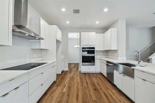 kitchen with visible vents, double wall oven, black electric stovetop, wall chimney range hood, and stainless steel dishwasher