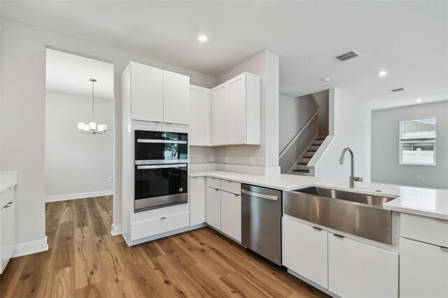 kitchen featuring visible vents, white cabinets, dishwasher, multiple ovens, and a sink