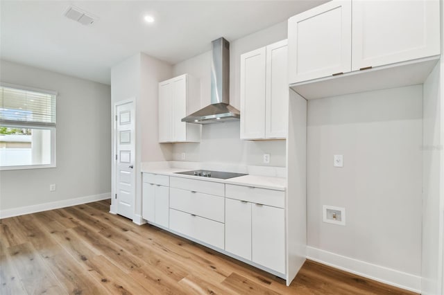 kitchen featuring wall chimney range hood, visible vents, baseboards, and black electric cooktop