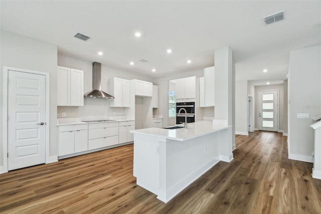 kitchen with black electric stovetop, wall chimney exhaust hood, visible vents, and a sink