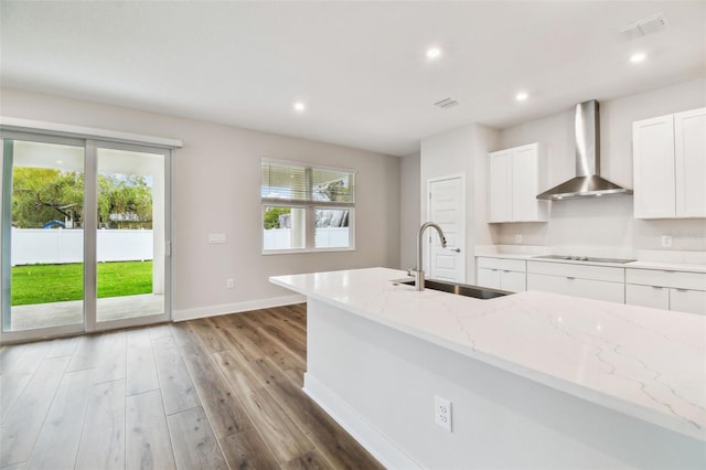 kitchen featuring wood finished floors, black electric stovetop, wall chimney range hood, white cabinetry, and a sink