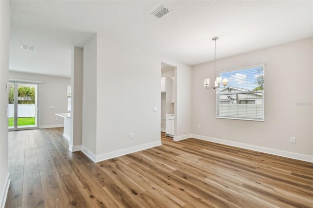 unfurnished dining area featuring a notable chandelier, wood finished floors, visible vents, and baseboards