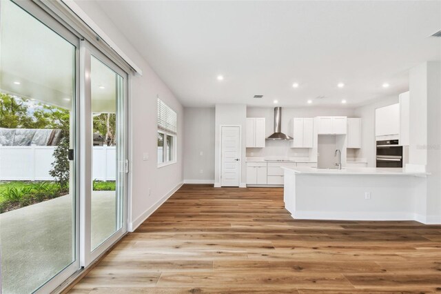 kitchen featuring a sink, white cabinetry, light wood-style floors, light countertops, and wall chimney range hood