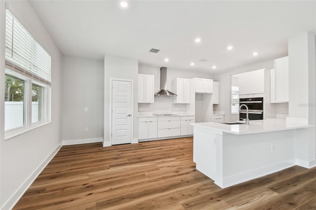 kitchen with visible vents, a sink, light wood-type flooring, a peninsula, and wall chimney exhaust hood