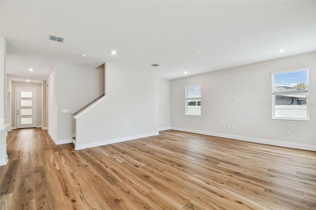 unfurnished room featuring light wood-type flooring, visible vents, a healthy amount of sunlight, and stairway