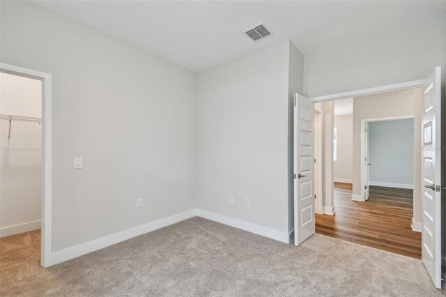 unfurnished bedroom with carpet, visible vents, a walk in closet, and baseboards