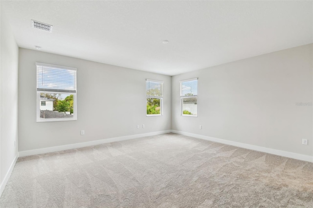 empty room featuring light carpet, visible vents, and baseboards