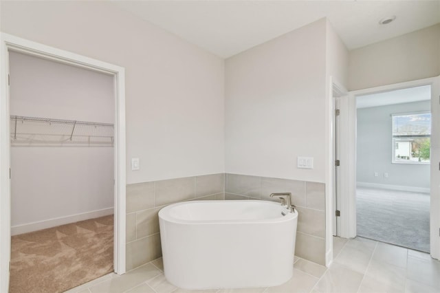 full bathroom featuring tile patterned flooring, a spacious closet, tile walls, and a freestanding bath