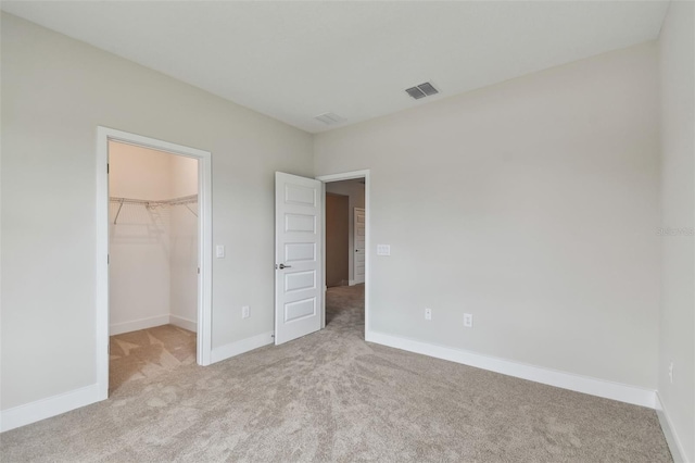 unfurnished bedroom with light carpet, visible vents, baseboards, a closet, and a walk in closet