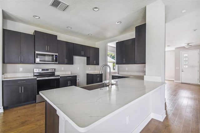 kitchen featuring kitchen peninsula, light stone counters, stainless steel appliances, sink, and dark hardwood / wood-style floors